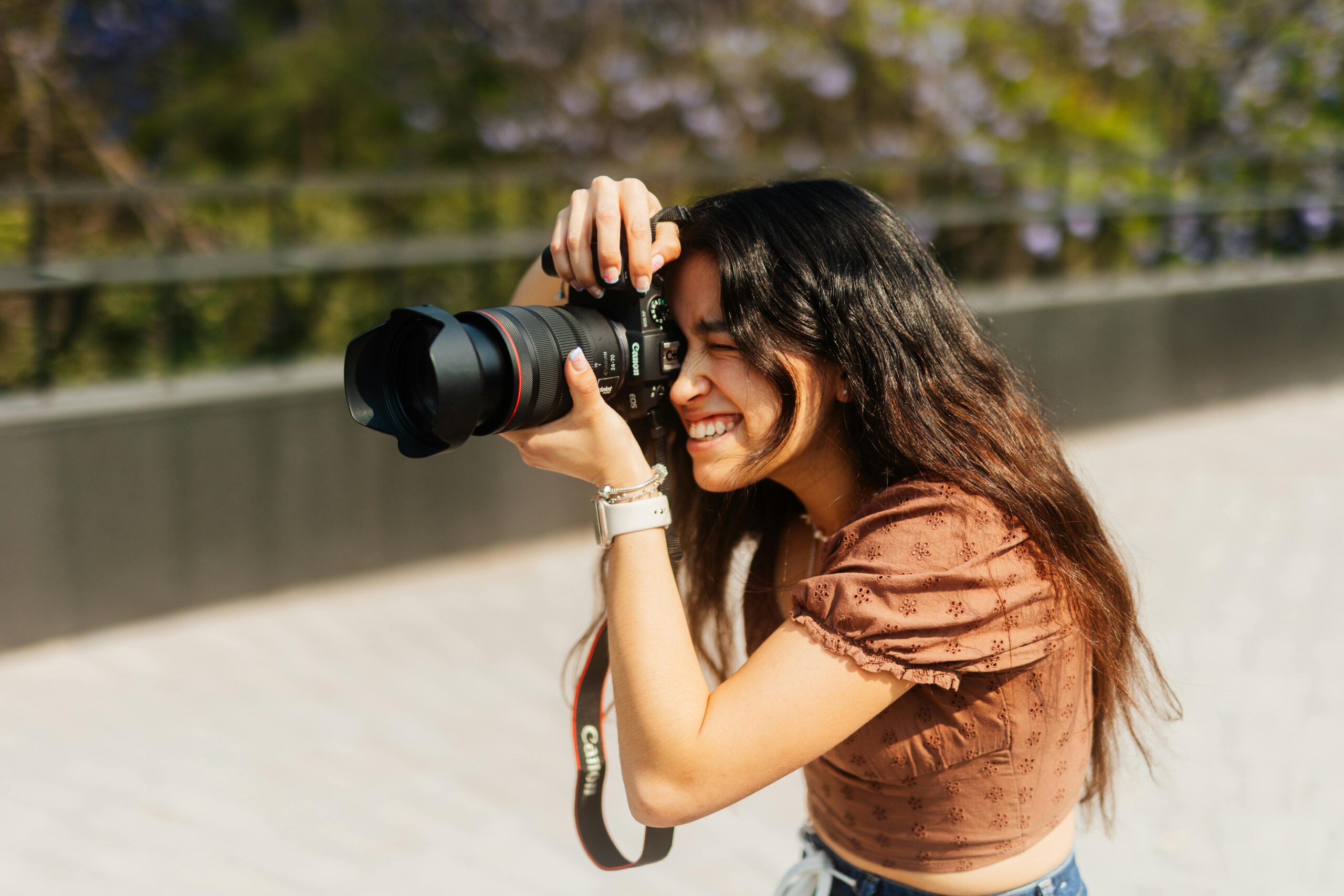 Smiling young woman captures a moment outdoors with a DSLR camera, embracing her passion.